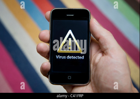Close up of male hand holding an iPhone which is indicating the detection of a virus. (Editorial use only). Stock Photo
