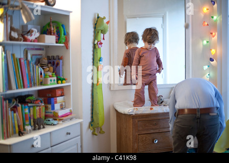 Toddler boy standing on top of changing table in nursery Stock Photo