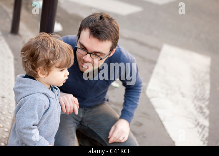 Father crouching beside toddler son, holding his hand Stock Photo