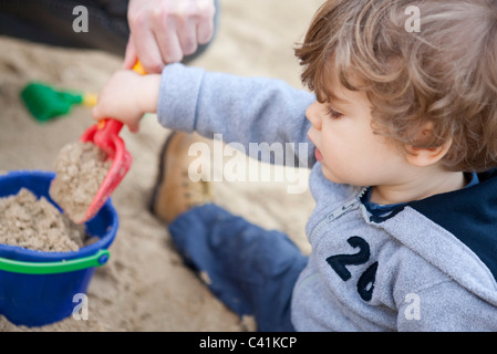 Toddler boy shoveling sand into bucket