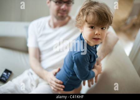 Toddler boy on couch with father, looking at camera Stock Photo