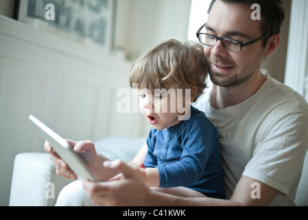 Toddler boy watching father using digital tablet with surprised expression Stock Photo