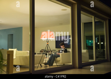 Man using laptop in living room, viewed through window Stock Photo