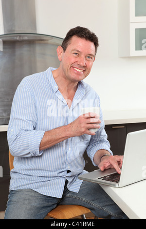 Man smiling looking to camera using a laptop in the kitchen Stock Photo