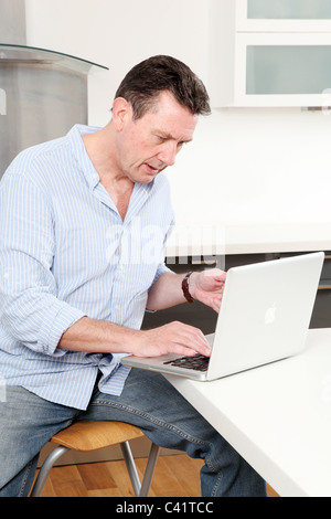 Man at home using his laptop in the kitchen. Stock Photo