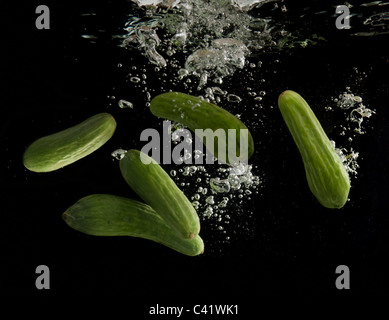 Fresh cucumbers are dropped into water on black background Stock Photo