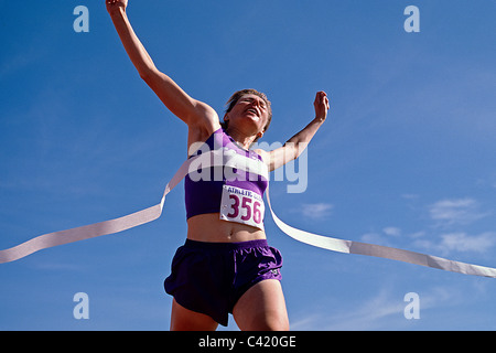 Female runner celebrates victory at the finish line. Stock Photo