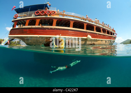 Split level, man diving next to the tour boat, Cleopatra island (Sedir Island), Aegean Sea, Turkey Stock Photo