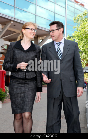 Man and woman wearing suits walking along talking. Stock Photo