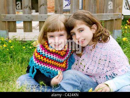 children sister girls smiling in meadow spring fence yellow flowers Stock Photo