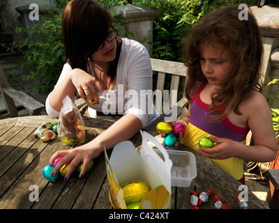 Young Girl And Teenage Aunt With Collection Of Chocolate Eggs After An Easter Egg Hunt In The Garden England Stock Photo
