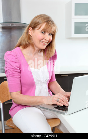 Cheeky woman using laptop, sitting in kitchen. Stock Photo