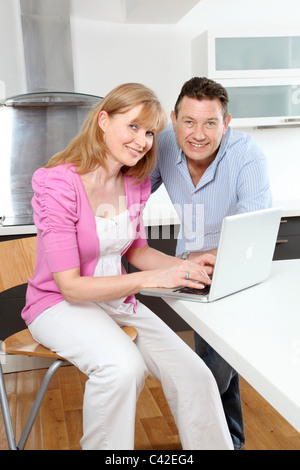 Couple smiling looking to camera using a laptop in the kitchen Stock Photo