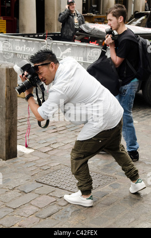 Asian male photographer taking a picture of a car at the Gumball rally 3000 Covent Garden London UK Stock Photo