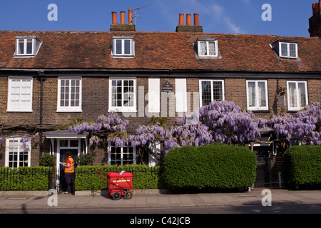 A post woman with a delivery trolley delivers post to Peg Woffington's House in Teddington High Street on sunny Spring morning Stock Photo