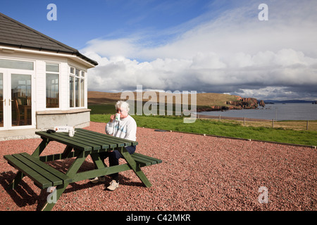 Female customer sat at a picnic table outside Braewick café in summer with a view along coastline. Eshaness Shetland Islands Scotland UK Stock Photo