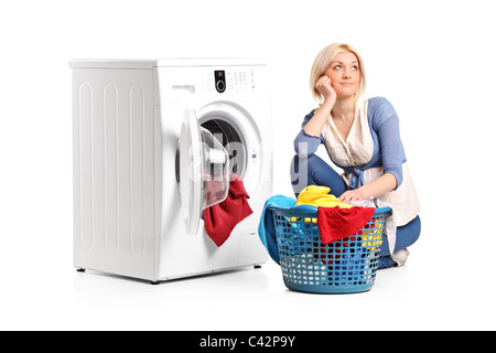 A young woman in thoughts with clothes seated next to a washing machine Stock Photo