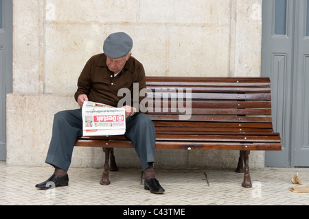 Old man reading newspaper on a public bench Stock Photo