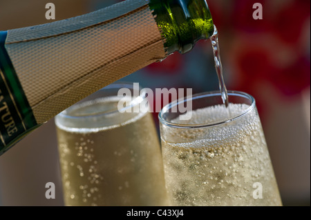 Sparkling Champagne pouring chilled glasses with bubbles of champagne on sunlit terrace with colourful Bougainvillea flowers and pool in background Stock Photo