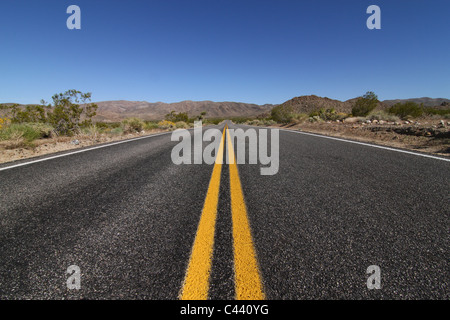 A view of the open road running through a wide expanse of empty desert. Stock Photo