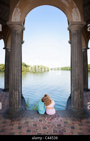 Two children sitting together under an arch next to a lake Stock Photo