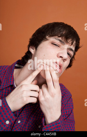 A teenage boy popping a zit on his face, portrait, studio shot Stock Photo