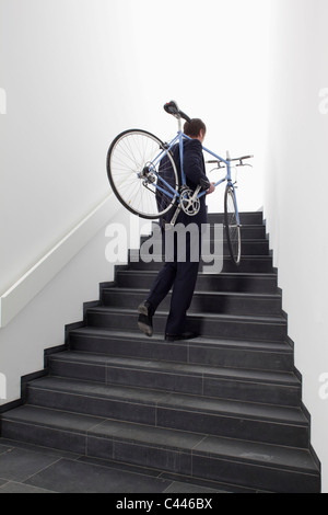 Business man returns home carrying bicycle up steps. Stock Photo