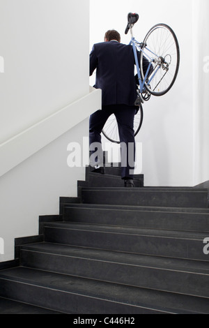 Businessman returns home carrying his bicycle up steps Stock Photo