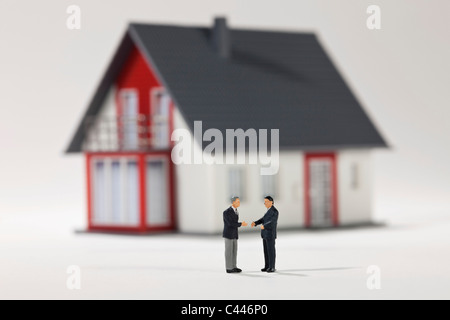 Two miniature businessmen figurines shaking hands in front of a house Stock Photo