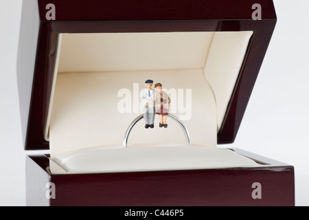 Miniature figurines of a senior woman and senior man sitting together on a wedding ring Stock Photo