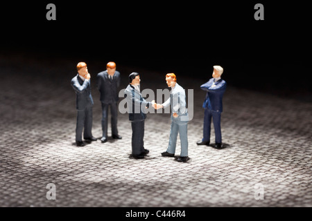 Two miniature businessmen figurines shaking hands amongst other businessmen figurines Stock Photo