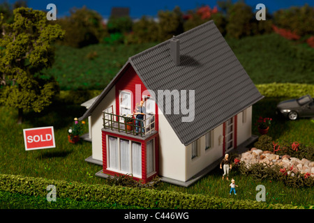 A diorama of a miniature house with a family of figurines and a SOLD sign Stock Photo