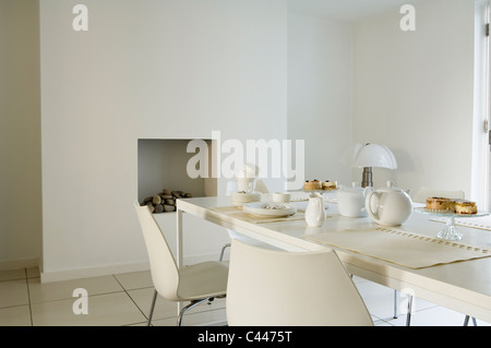 Minimal modern dining area with white table and chairs and open fireplace Stock Photo