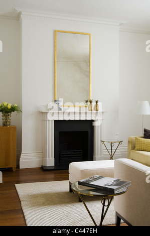 Gilt mirror above mantelpiece in living room with rug and ottoman Stock Photo