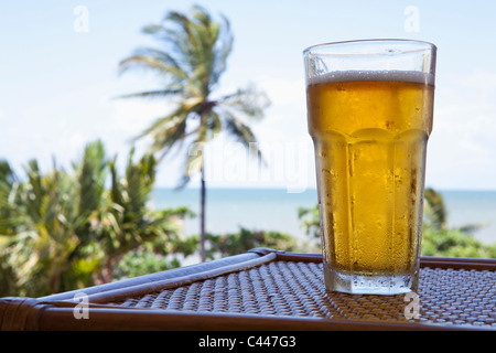 A glass of cold beer on a table with a view of a beach Stock Photo