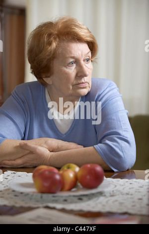 A senior woman sitting at a table looking sad Stock Photo