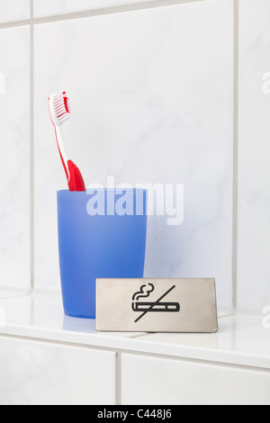 A no smoking sign next to a toothbrush in a cup Stock Photo