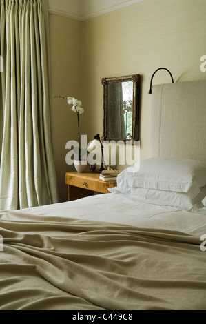 Bedroom with thick floor length curtains, unmade bed with silk linen and bedside table Stock Photo