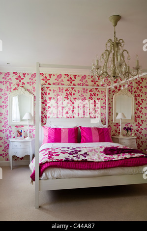 White fourposter bed in bedroom with Designer's Guild pink floral patterned wallpaper and chandelier Stock Photo