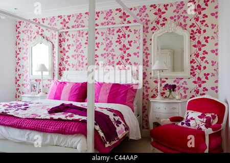 Red velvet armchair in bedroom with fourposter bed and Designers Guild floral pink wallpaper Stock Photo