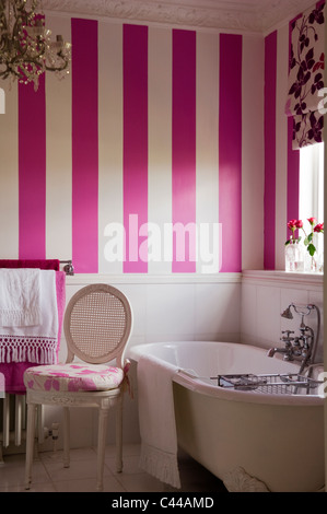 Freestanding bath tub in bathroom with striped wallpaper and floral blinds Stock Photo