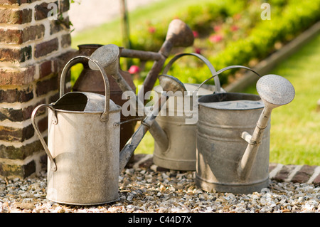 Old fashioned watering cans on gravel by lawn in garden Stock Photo