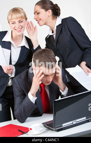 Photo of thinking boss in front of laptop while one of his employees whispering something to another woman Stock Photo