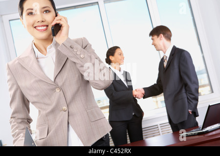 Portrait of happy woman calling on the phone on the background of business people’s handshake Stock Photo