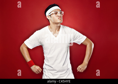 Studio portrait of Asian male teenager doing a superhero pose in white athletic gear & nerdy glasses against a red backdrop. Stock Photo