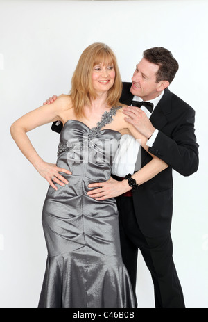 Woman wearing long formal dress hands on hips, man hands on her shoulders, both looking at each other with cheeky smiles Stock Photo
