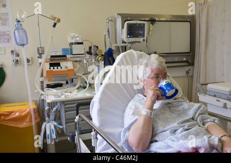 Senior woman patient drinking tea recovering in Resuscitation unit in Accident and Emergency department of a hospital after a heart attack. Wales, UK. Stock Photo