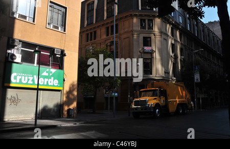 Urban building shade view of yellow garbage truck parked by grey shutters closed pharmacy, San Antonio Street, Santiago, Chile Stock Photo