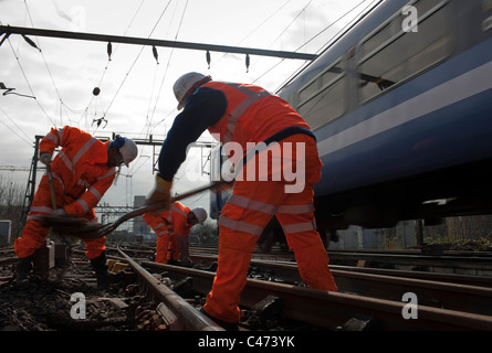 Railway workers in orange high visibility clothing repairing a commuter railway line in London with moving train in background Stock Photo