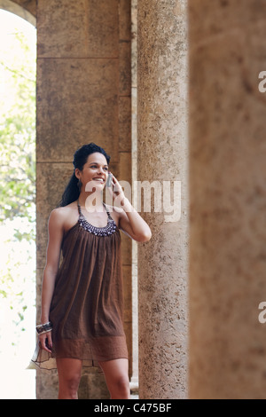 mid adult hispanic woman talking on mobile phone and leaning on columns outdoors. Vertical shape, front view Stock Photo